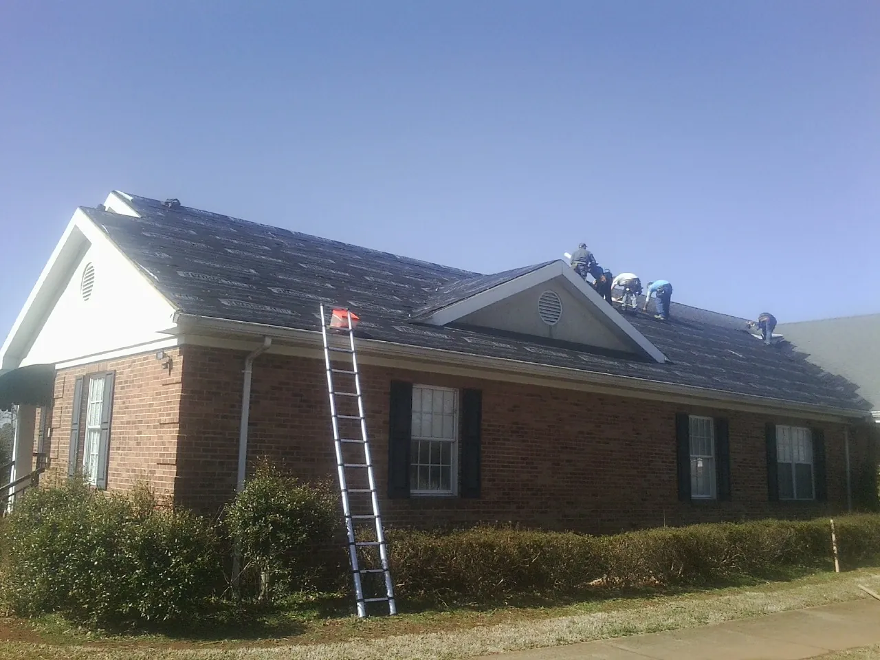 Crew tearing shingles off a brick ranch roof with a ladder set — Emergency Roof Repair work by our crew in Concord