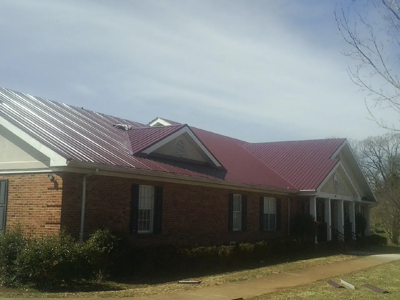 Red metal roof with gabled entries on a long brick building, from a Hail Damage Roof Repair job in Concord